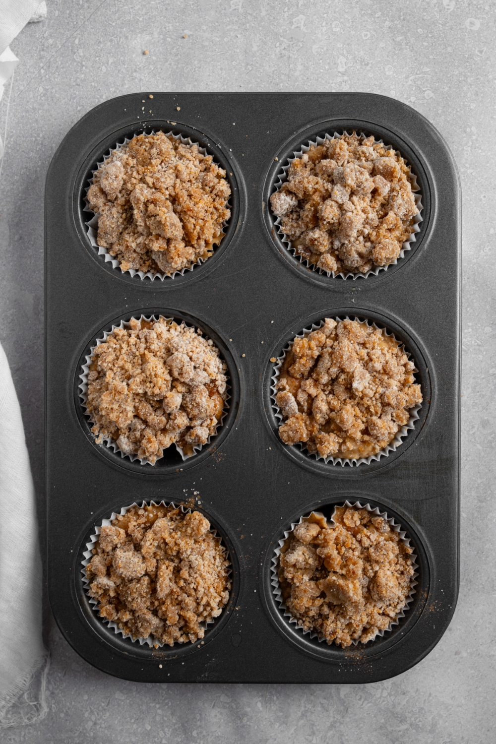 A muffin tin with uncooked coffee cake muffins.