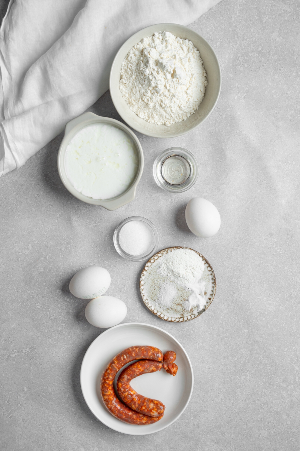 An overhead shot of several bowls in various sizes containing ingredients to make pancake tacos including flour, baking soda, baking powder, sausage links, eggs, buttermilk, and sugar.