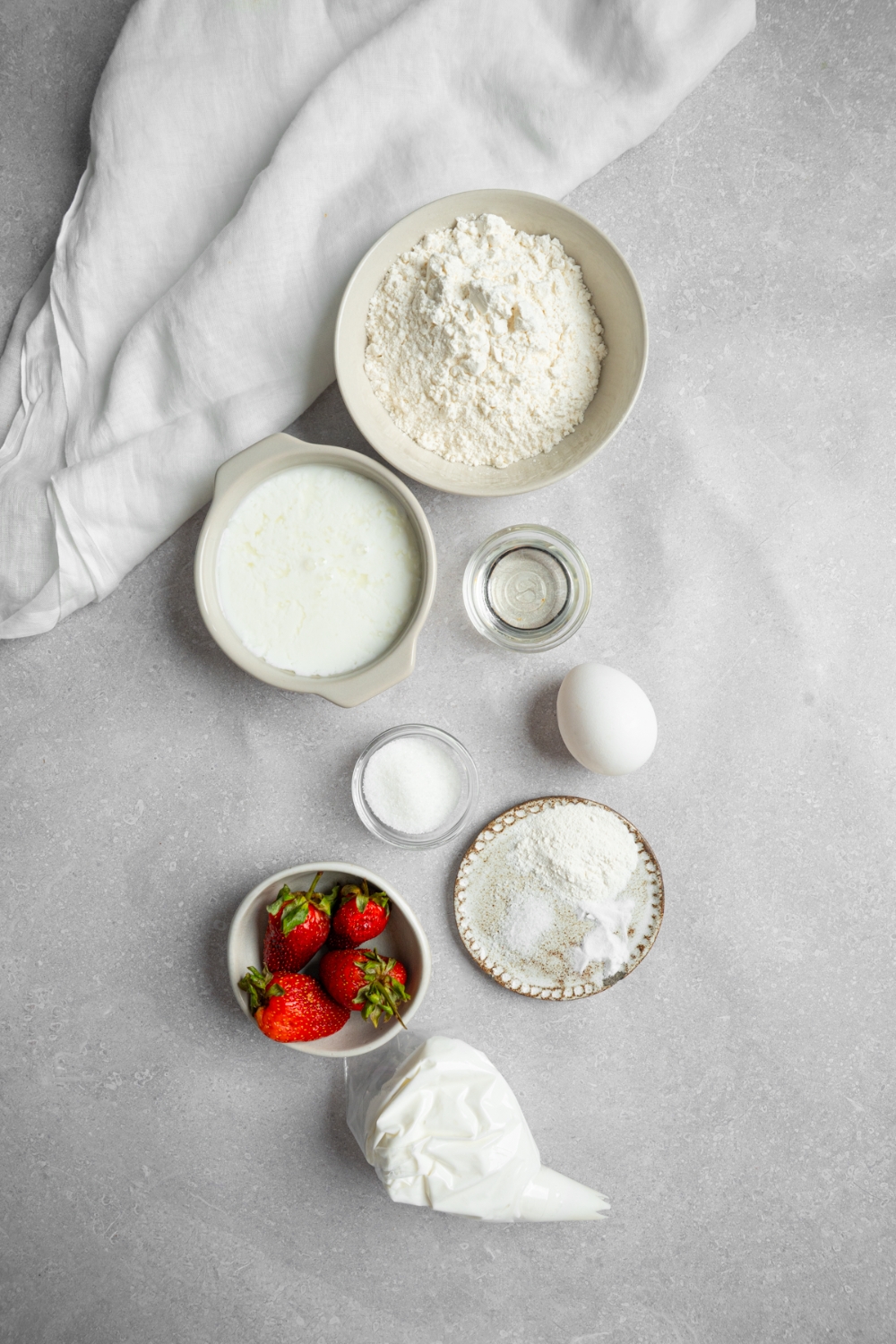 An overhead shot of several bowls in various sizes containing ingredients to make scrambled pancakes including flour, baking powder, baking soda, sugar, egg, buttermilk, and oil.