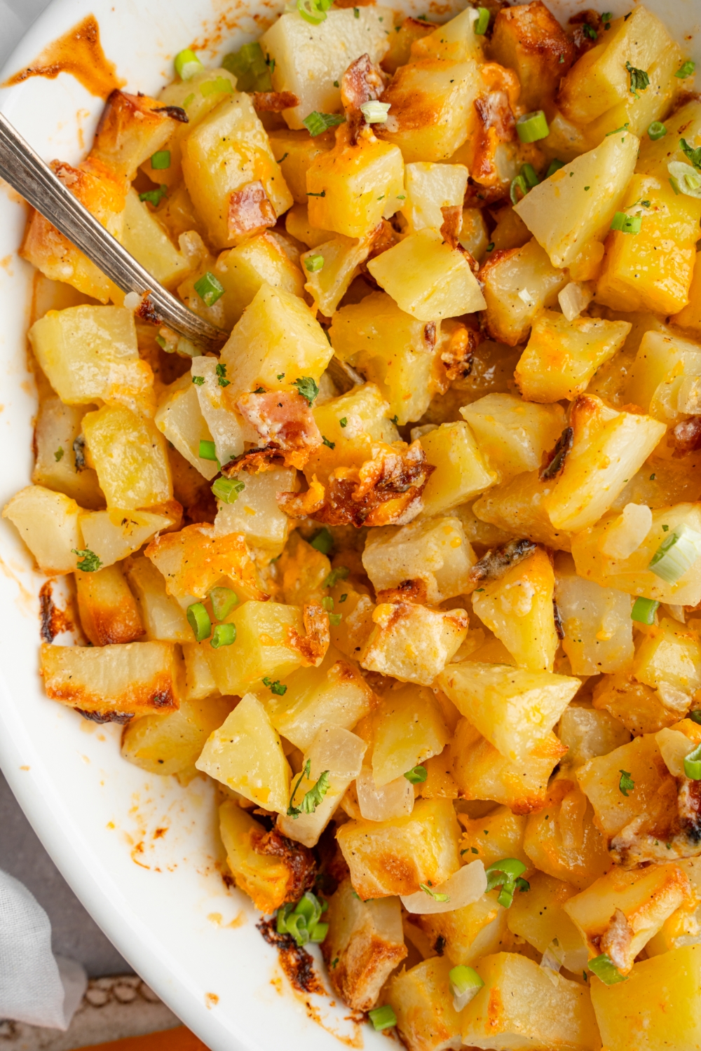 A baking dish with cheesy Mississippi mud potatoes garnished with sliced green onions. There is a spoon in the potatoes.