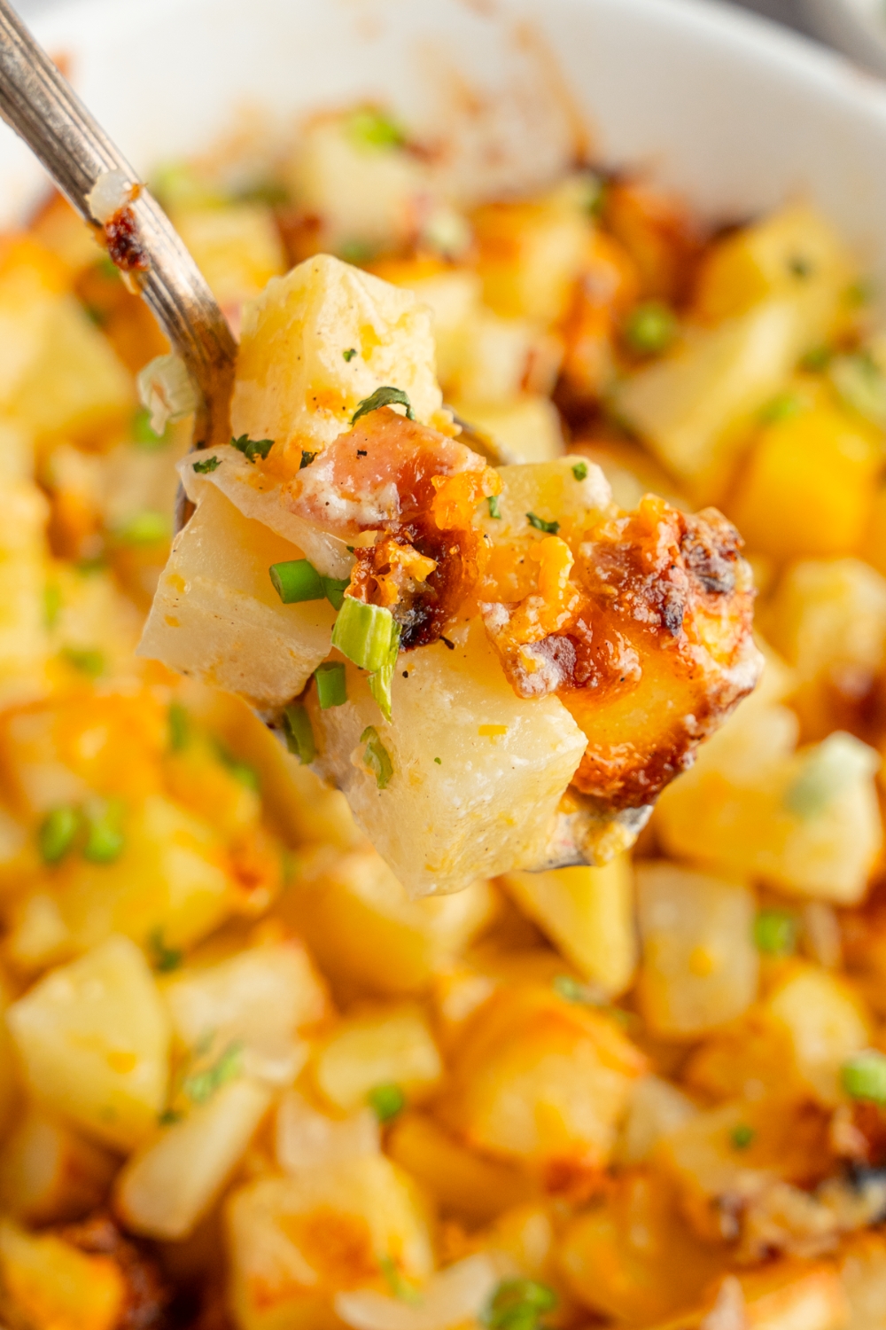 A close up of a fork with a bite of Mississippi mud potatoes with a baking dish of potatoes blurred in the background.
