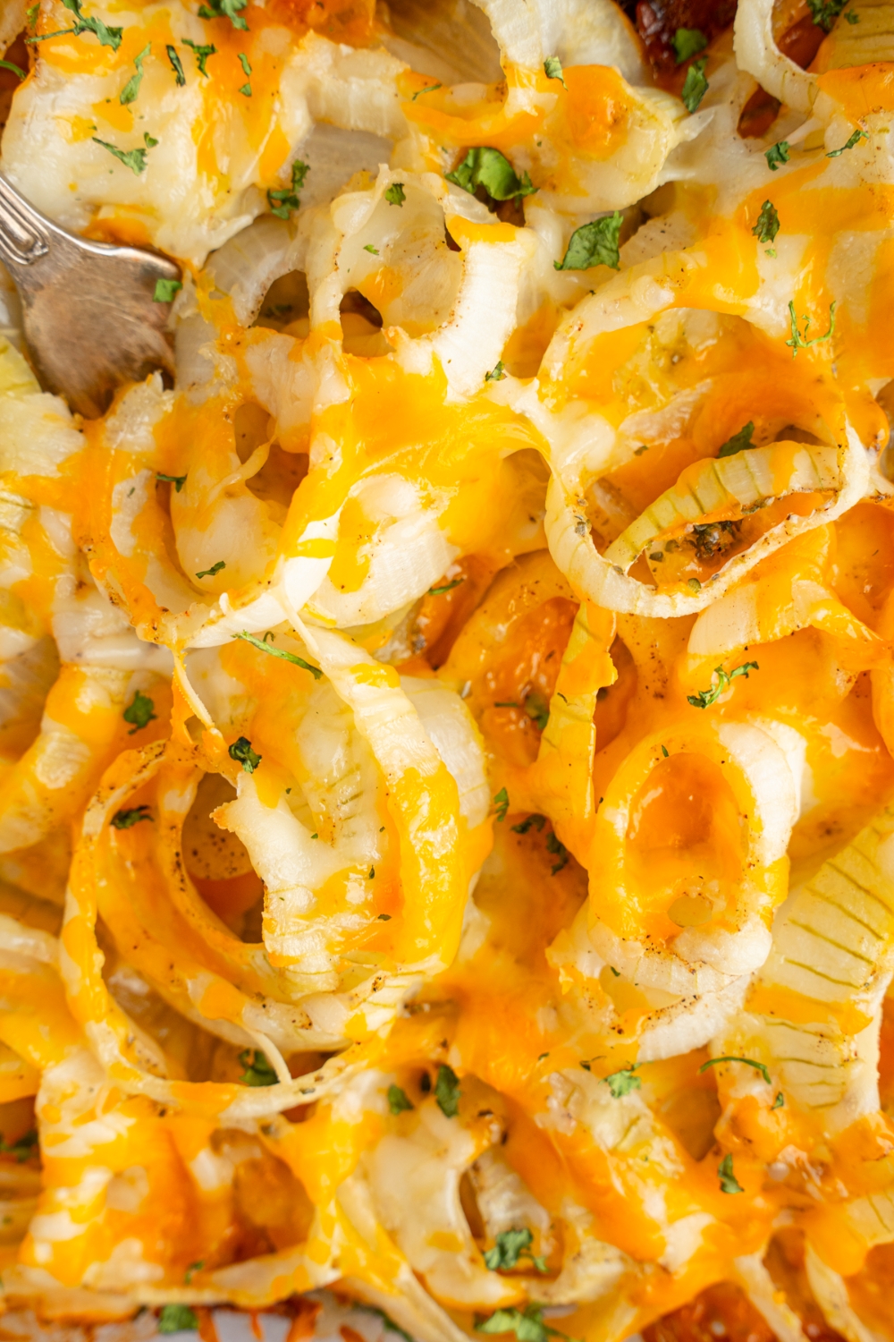 Tennessee onions baked with shredded cheese and garnished with fresh parsley. A fork is in the onions.