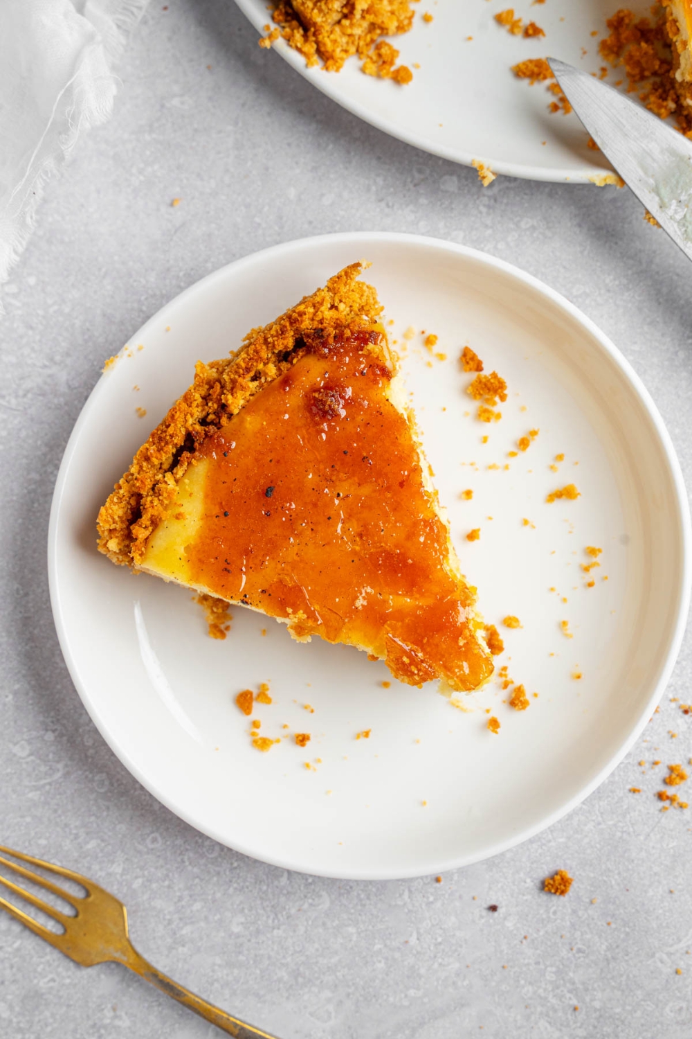 A white plate with a slice of creme brulee cheesecake. The plate is on a white counter with the remaining cheesecake and a fork.