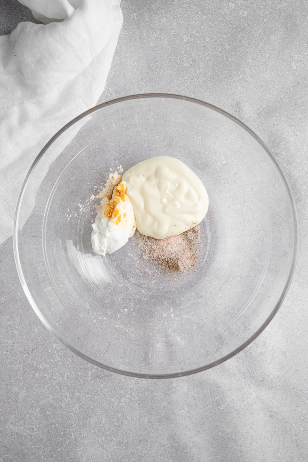 A glass bowl with mayo, sour cream, and seasonings. The bowl is on a white counter with a white cloth napkin.