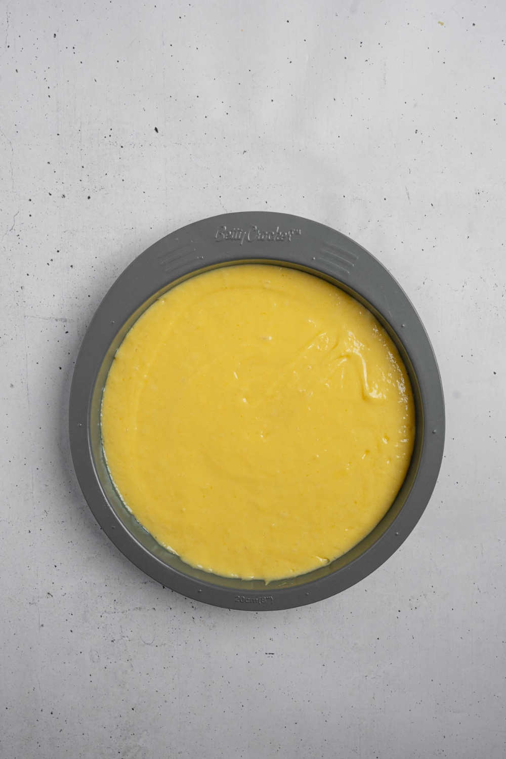 A cake tin with mango cake batter. The tin is on a white counter.