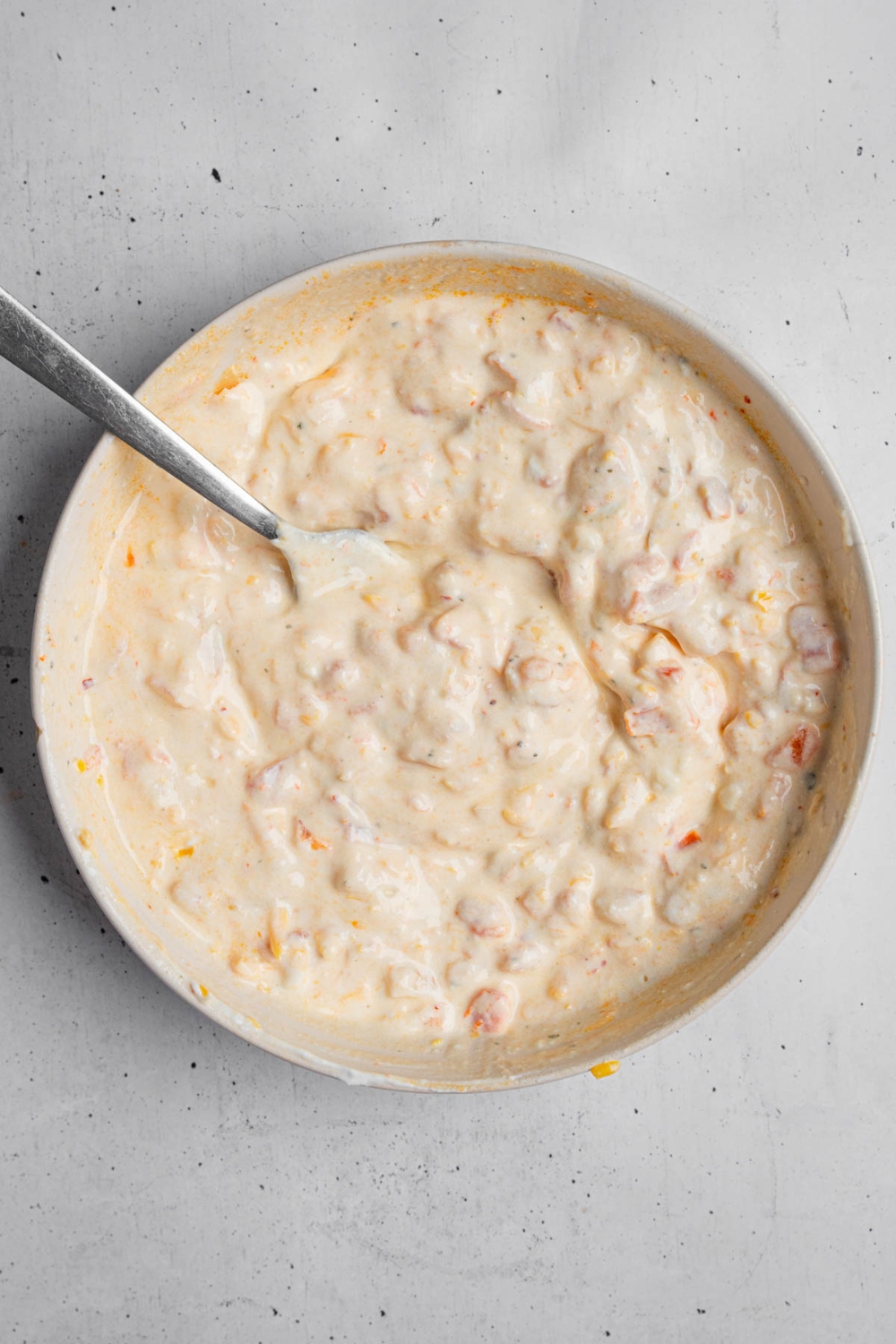 A white bowl with a spoon mixing ingredients to make boat dip. The bowl is on a white counter.