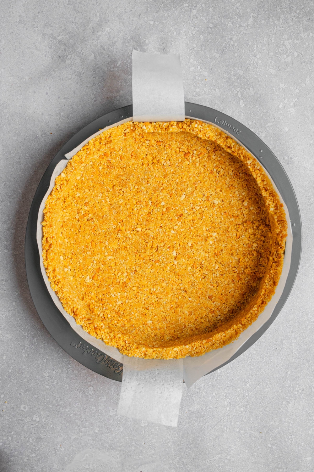 A graham cracker crumb crust on a pan. The pan is on a white counter.