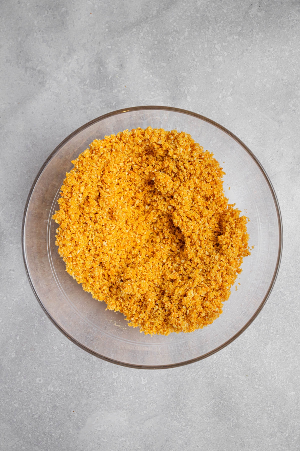 A glass bowl with a graham cracker crumb mixture. The bowl is on a white counter.