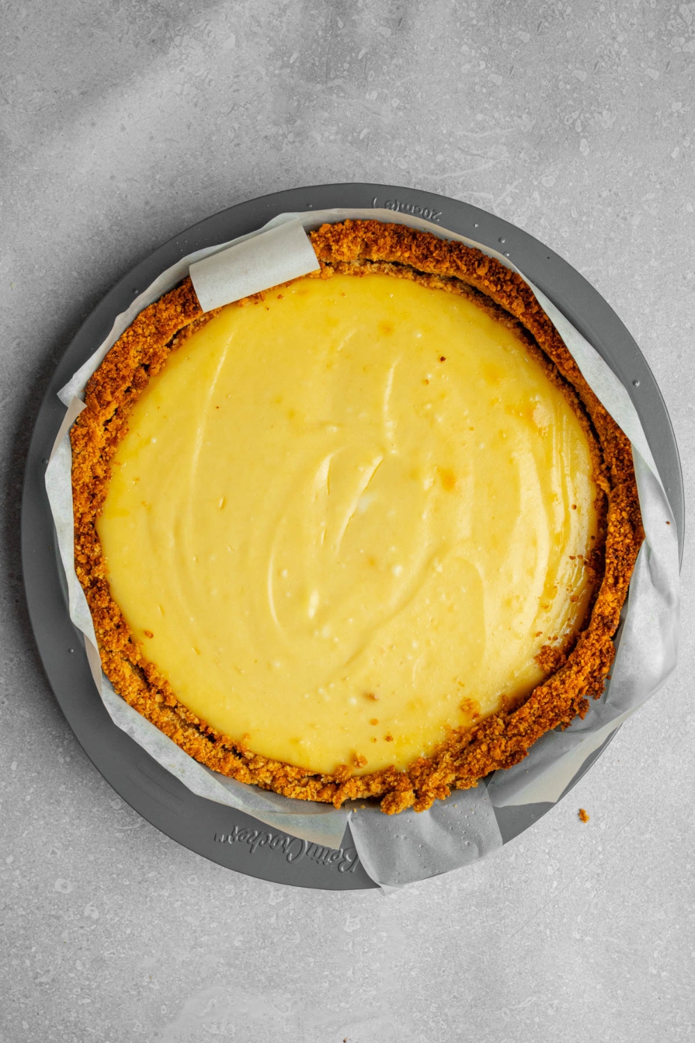 A cheesecake pan with cooled creme brulee cheesecake in a graham cracker crumb crust. The pan is on a white counter.