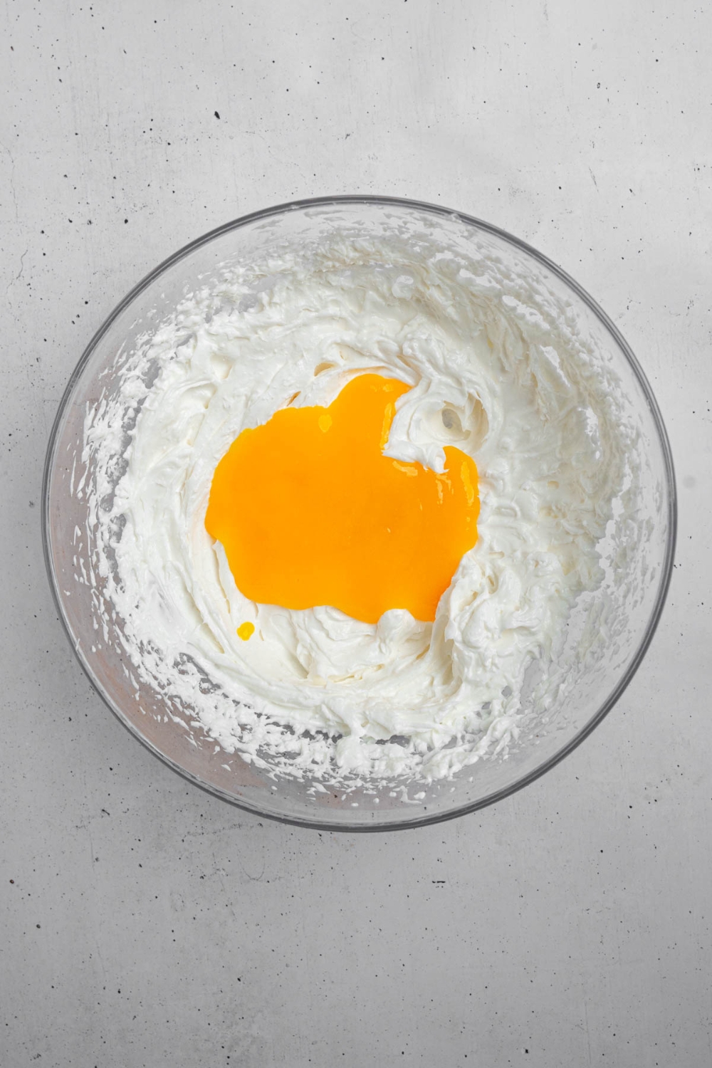 A glass bowl with whipped cream and mango puree. The bowl is on a white counter.