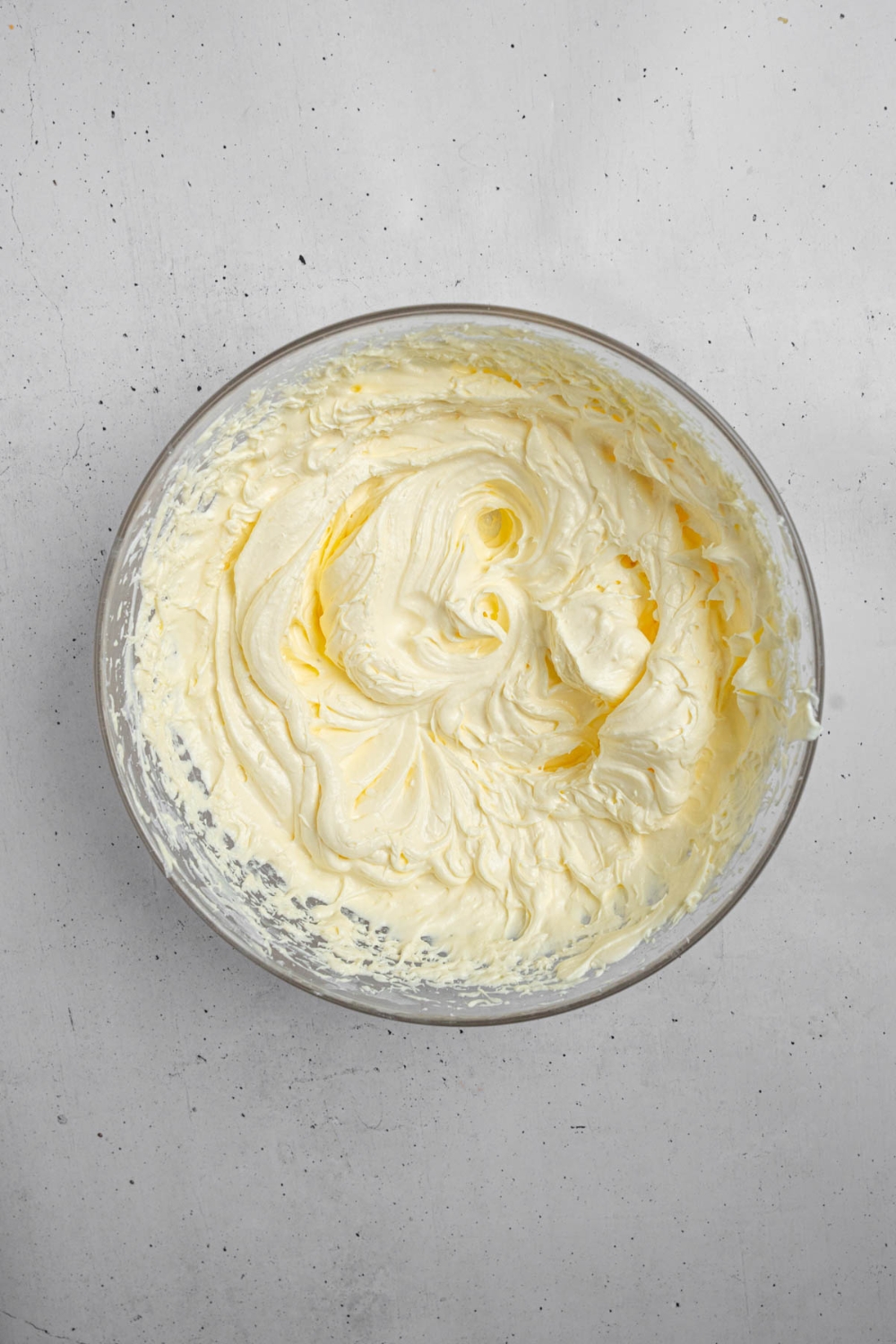 A glass bowl with a whipped cream and mango puree mixture. The bowl is on a white counter.