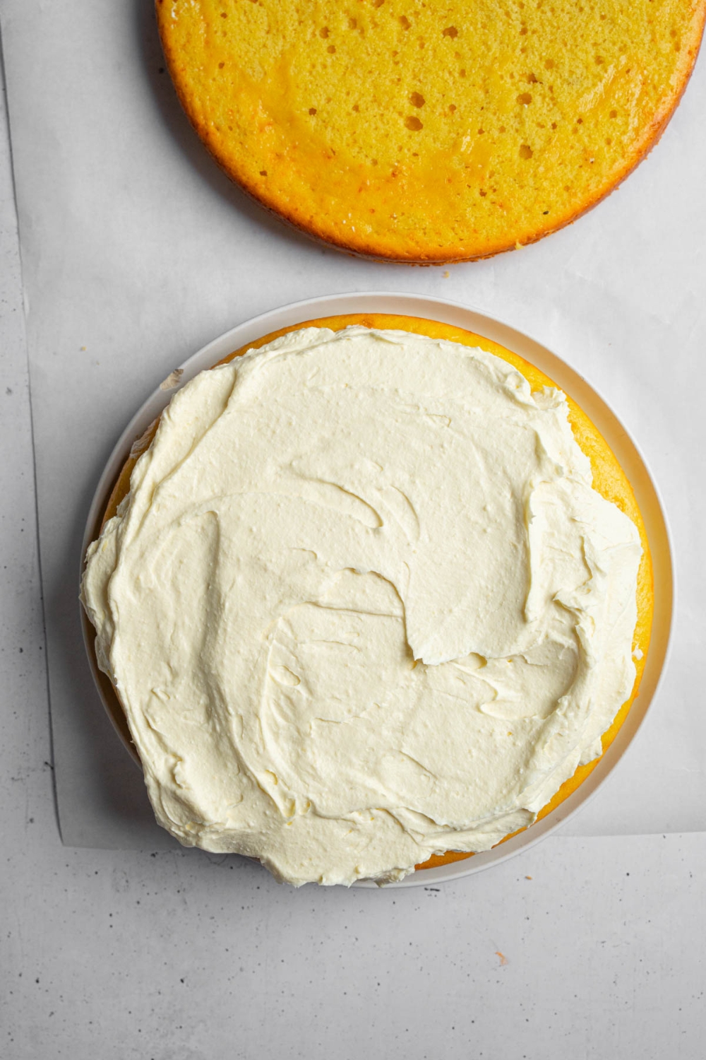 A layer of mango cake batter topped with a whipped mango mixture. The cake is on a piece of parchment paper.