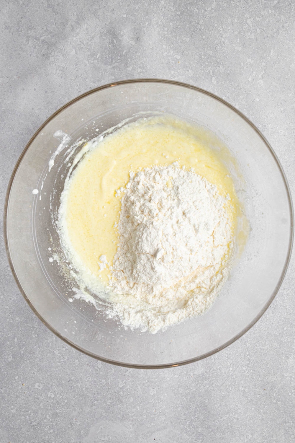 A glass bowl with dry ingredients on top of wet ingredients for mini pancake batter. The bowl is on a white counter.
