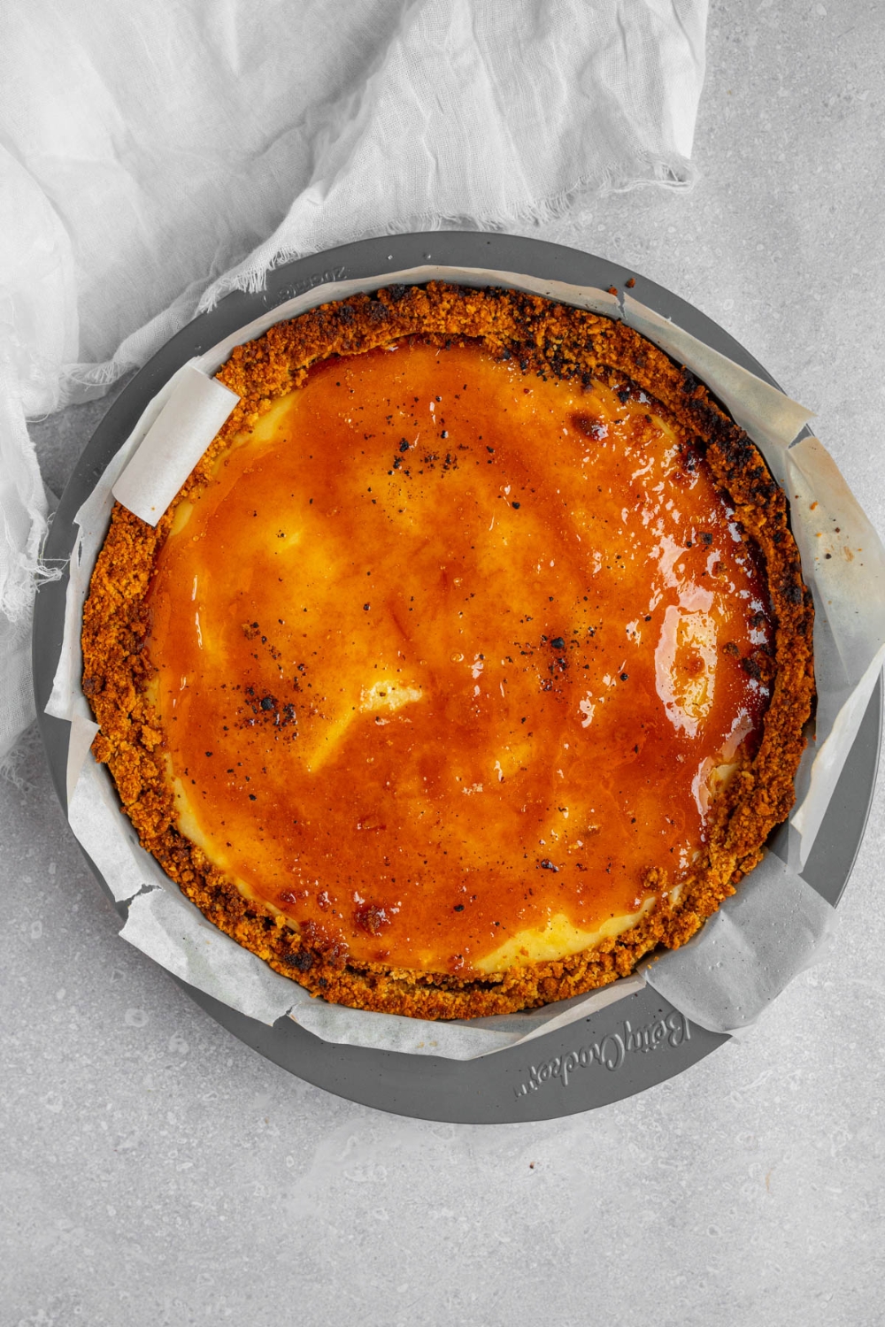 Creme brulee cheesecake in a pan lined with parchment paper. The pan is on a white counter with a white cloth napkin.