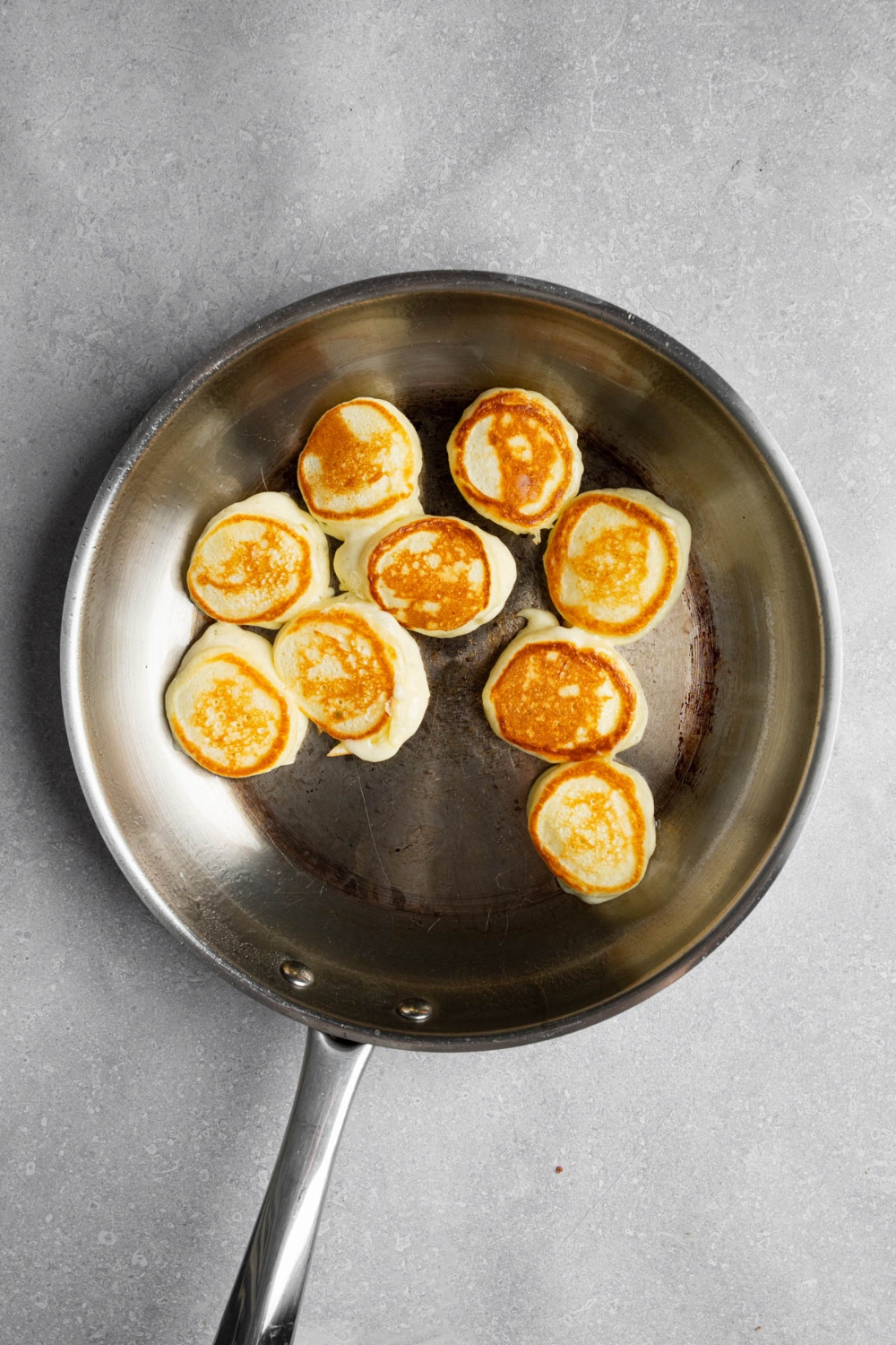 A stainless steel skillet with several cooked mini pancakes. The skillet is on a white counter.