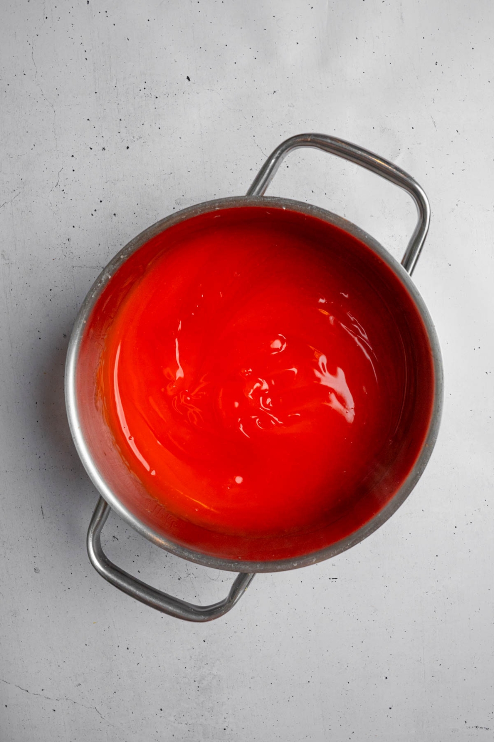 A stock pot with a cooked strawberry jello mixture. The pot is on a white counter.