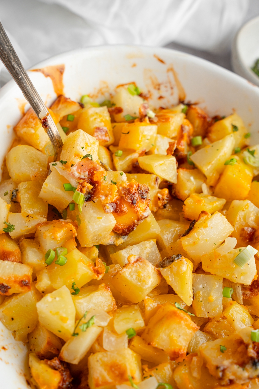 A baking dish with cheesy Mississippi mud potatoes garnished with sliced green onions. There is a spoon in the potatoes.