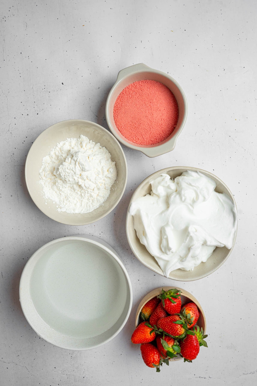 An overhead shot of several bowls in various sizes containing ingredients to make strawberry fluff salad including water, strawberry jello, vanilla pudding mix, cool whip, and strawberries.