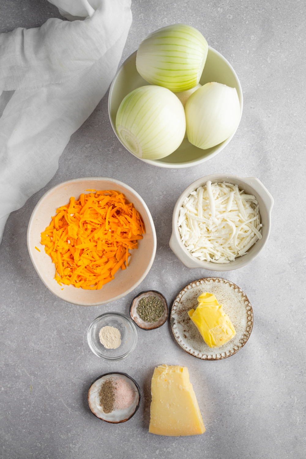 An overhead shot of several bowls in various sizes containing ingredients to make Tennessee onions including onions, shredded cheddar cheese, shredded mozzarella cheese, butter, and seasonings.