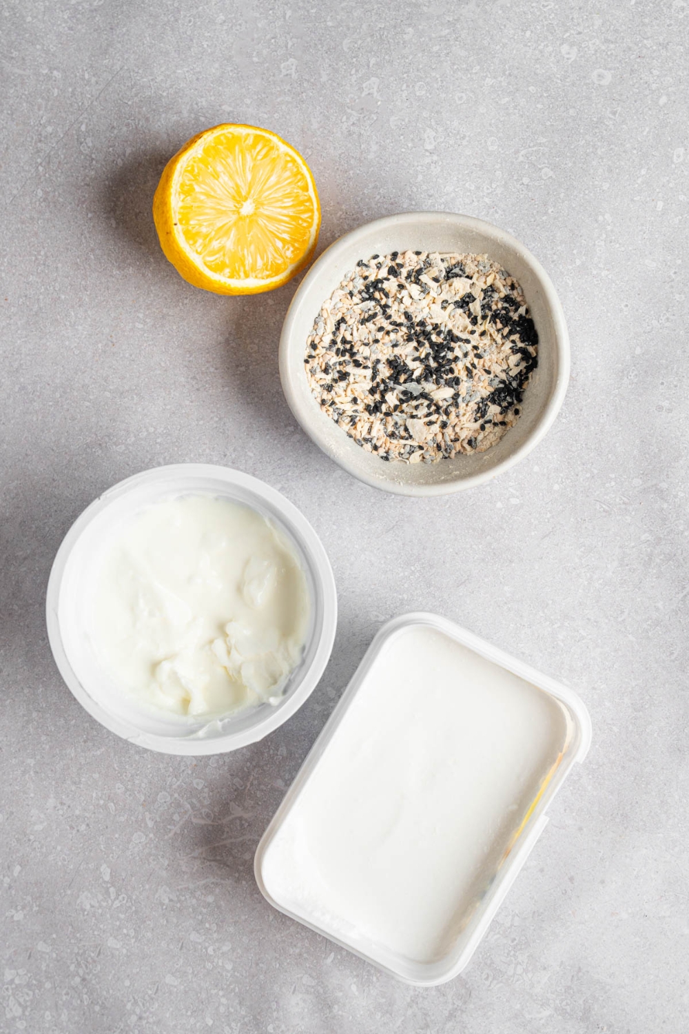 An overhead shot of several ingredients to make bagel dip including greek yogurt, cream cheese, everything bagel seasoning, and lemon.