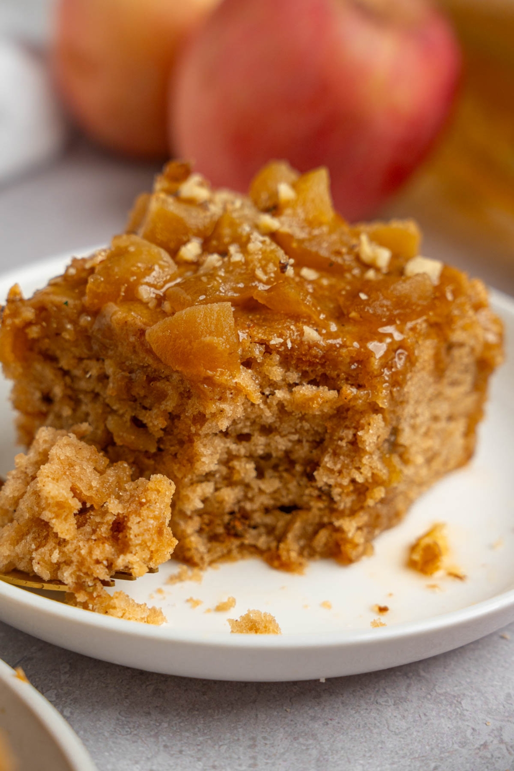 A slice of Amish applesauce cake topped with chopped walnuts with a bite taken from it. The cake is on a white plate.