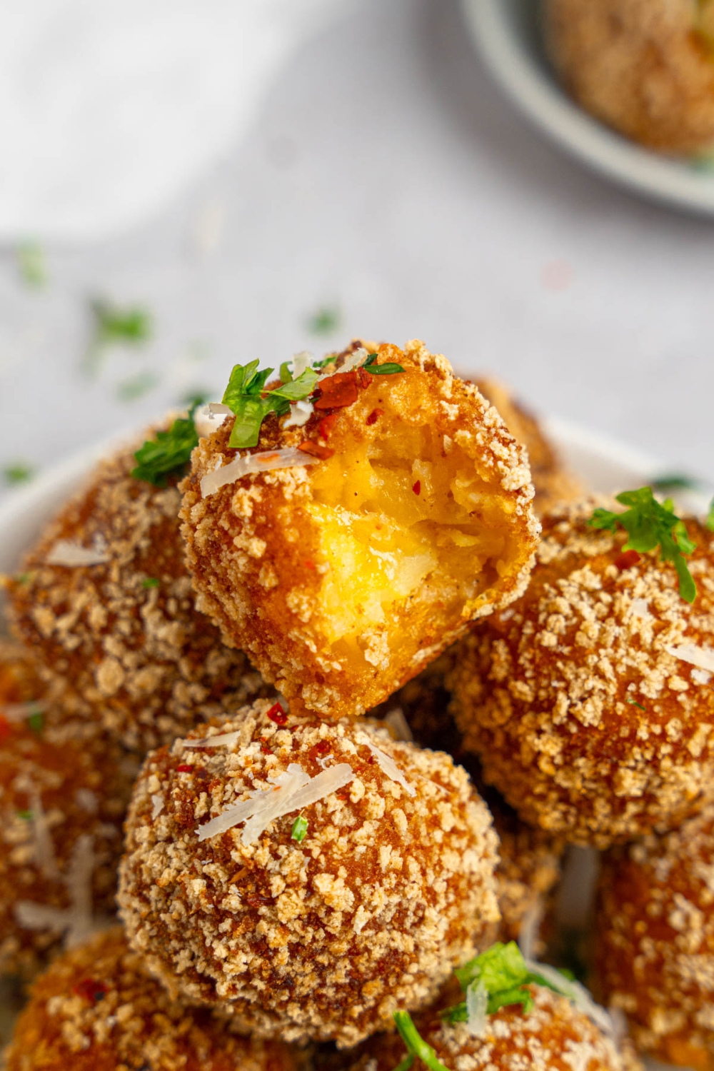 A pile of cheesy mashed potato balls garnished with fresh parsley and shredded cheese. The top ball has a bite taken from it.