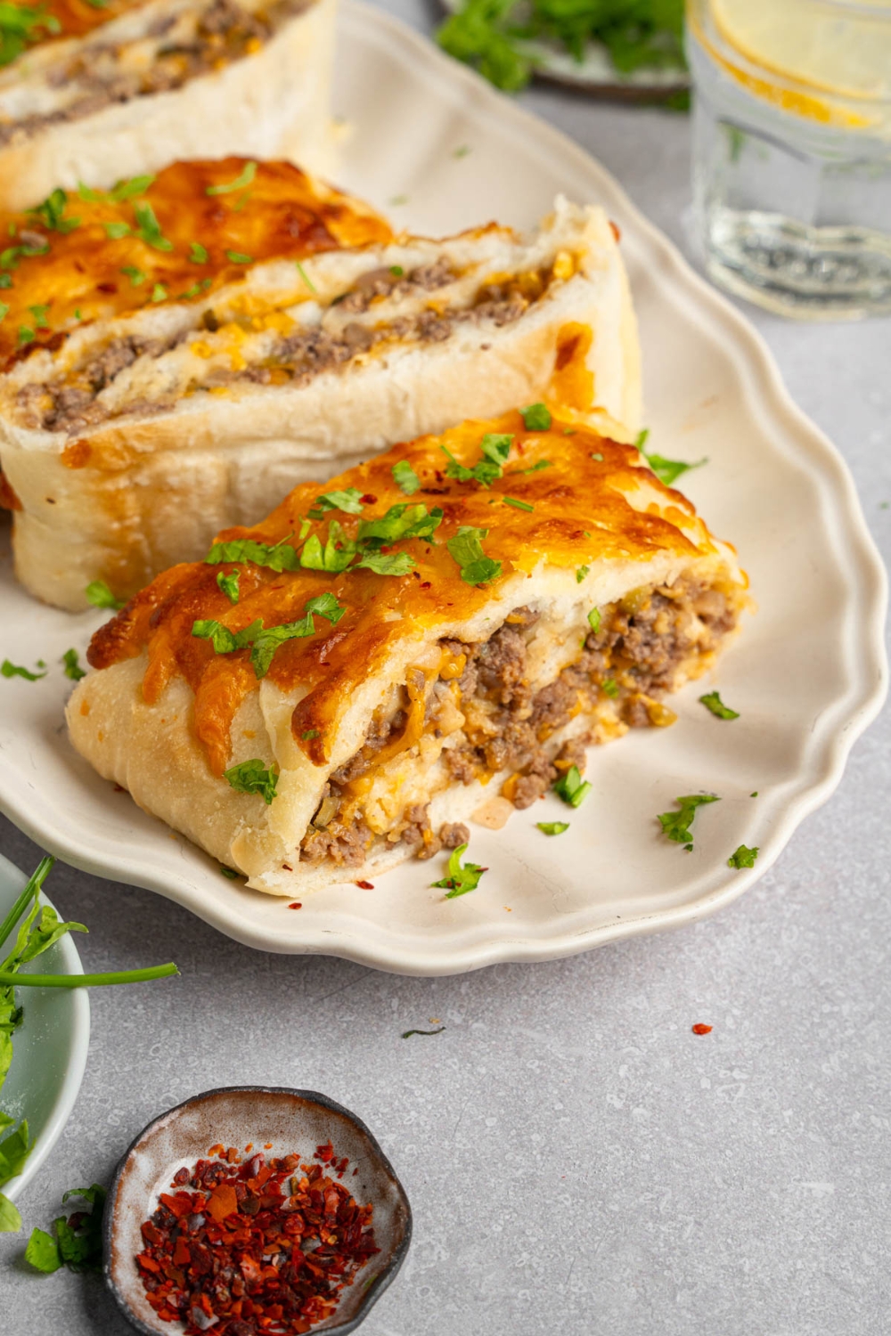 Slices of garbage bread served on a white platter garnished with chopped parsley. The platter is on a white counter with a small ramekin of garnishes.