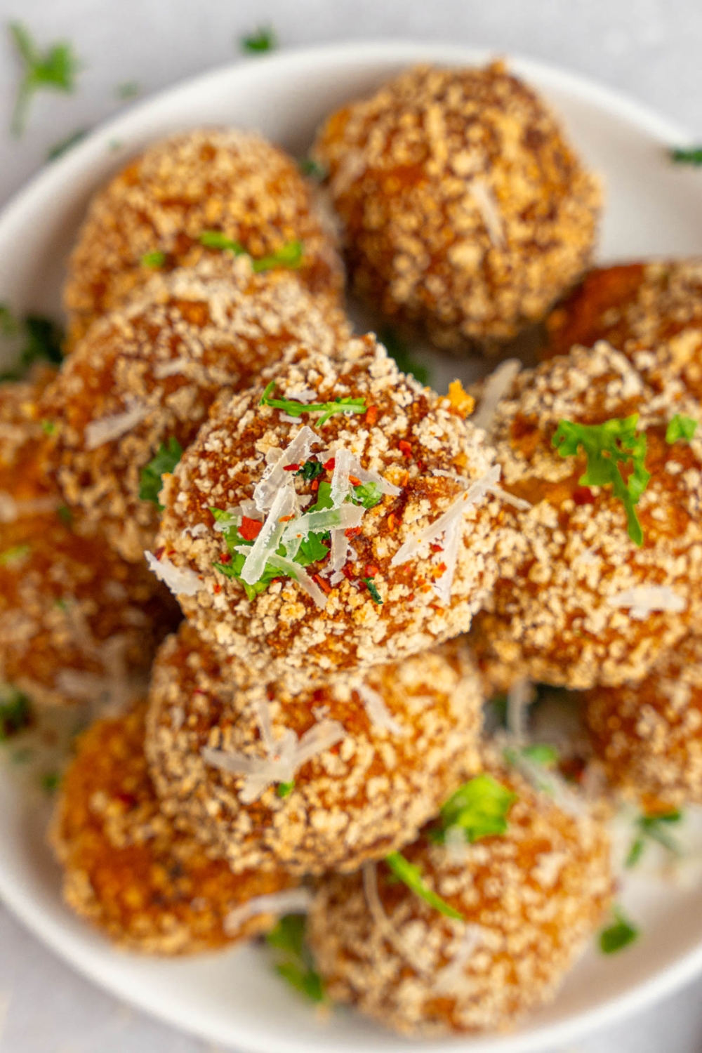 A pile of cheesy mashed potato balls served on a white plate garnished with fresh parsley and cheese.