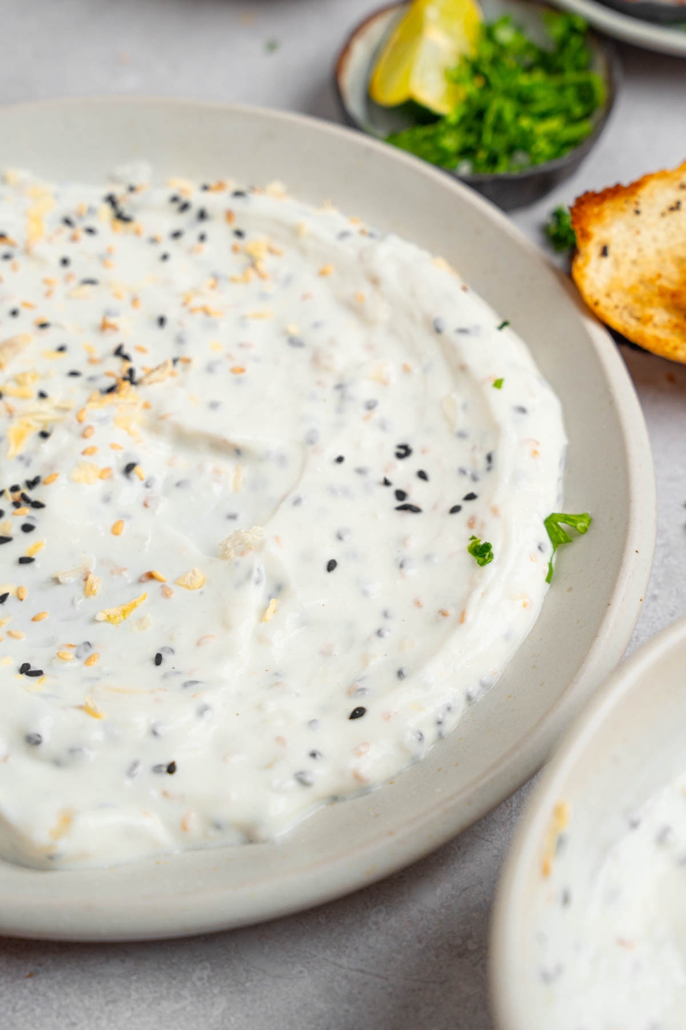 Bagel dip served in a white plate on a white counter with toasted bread and small ramekins of garnishes.