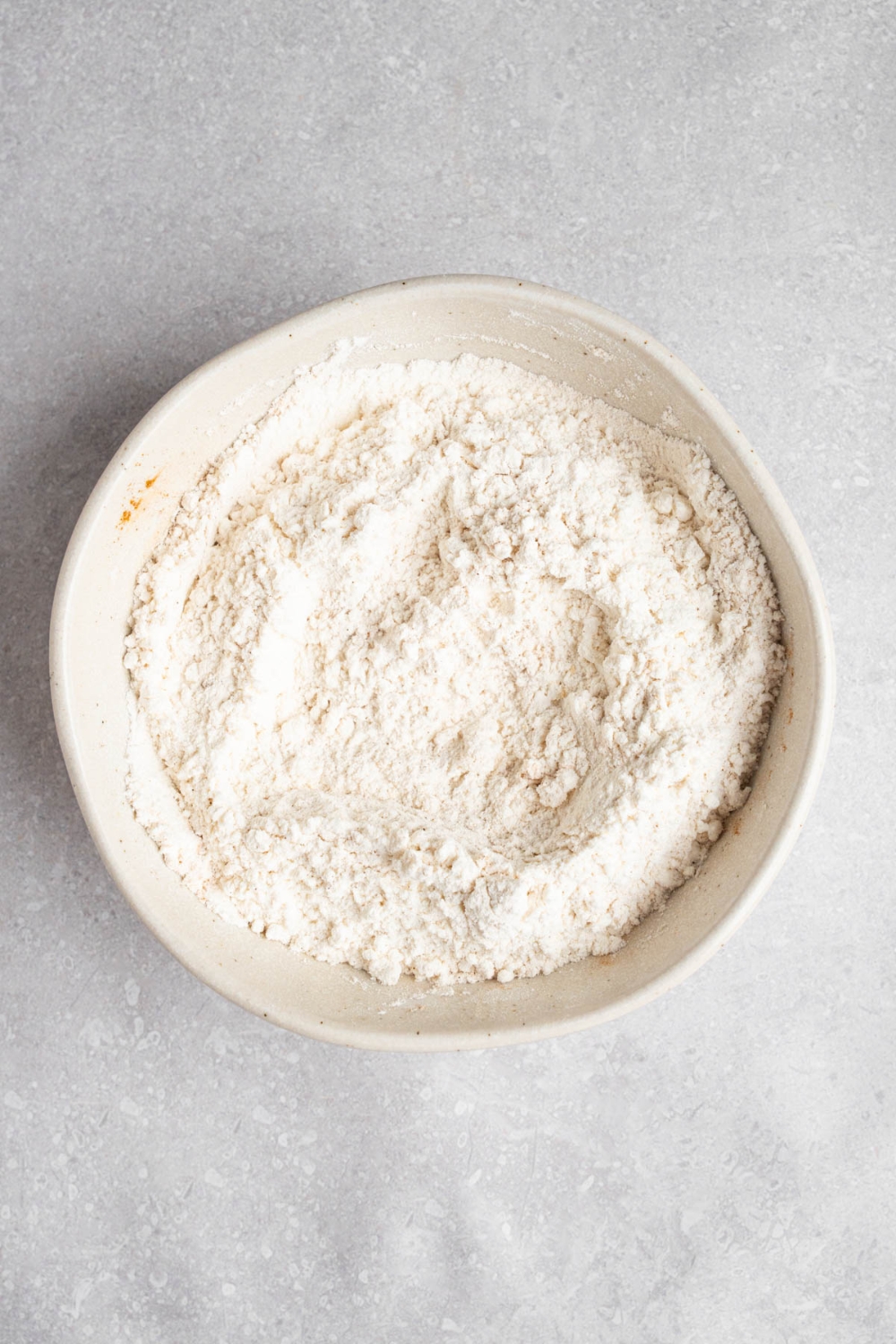 A white bowl with dry ingredients to make Amish applesauce cake. The bowl is on a white counter.