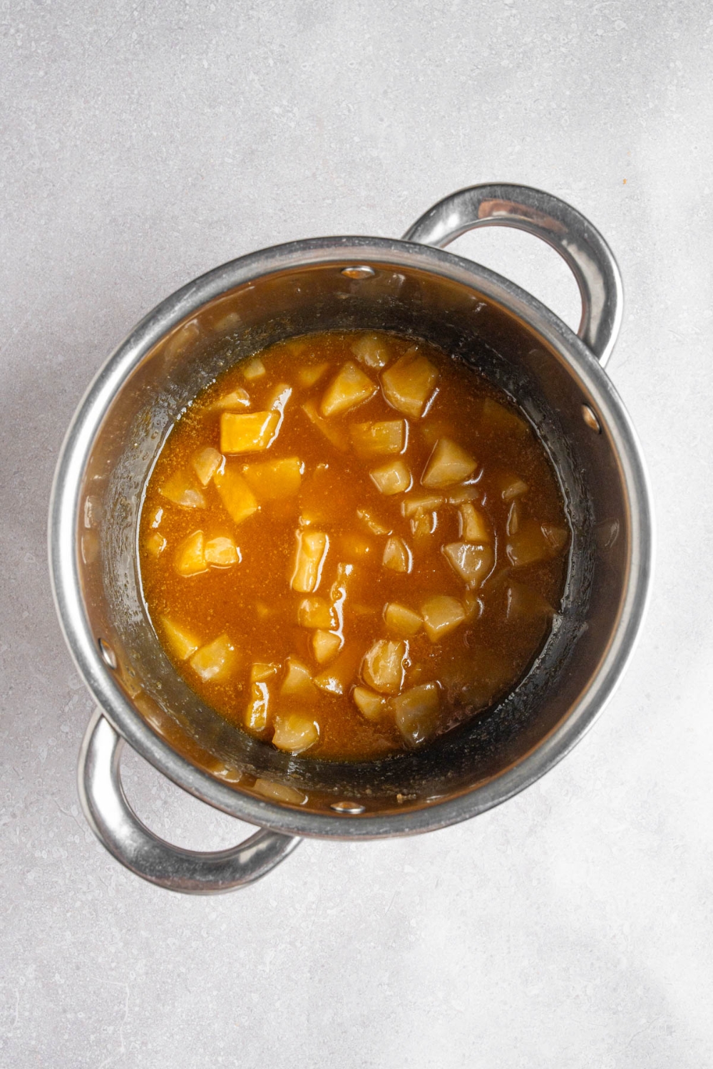 A steel pot with stewed apples in a caramel glaze. The pot is on a white counter.