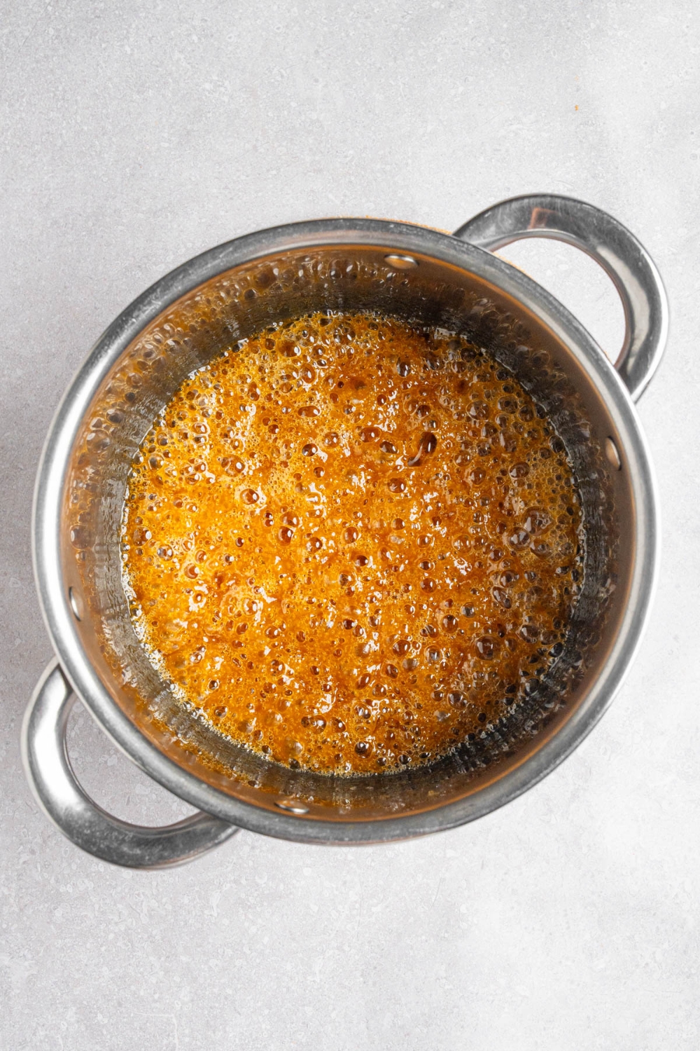A steel pot with a cooked caramel glaze. The pot is on a white counter.