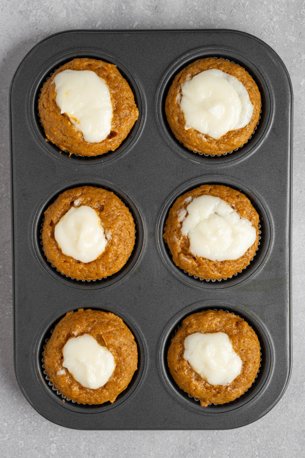 A muffin tray with six baked copycat Starbucks pumpkin muffins topped with cream cheese filling. The tray is on a white counter.