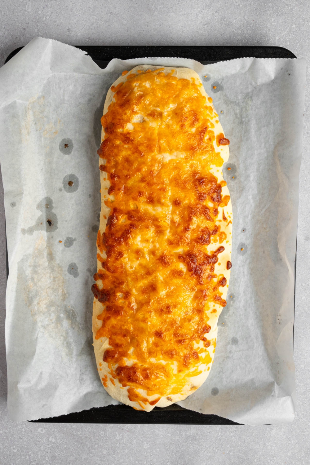 A loaf of baked garbage bread on a baking sheet lined with parchment paper. The baking sheet is on a white counter.