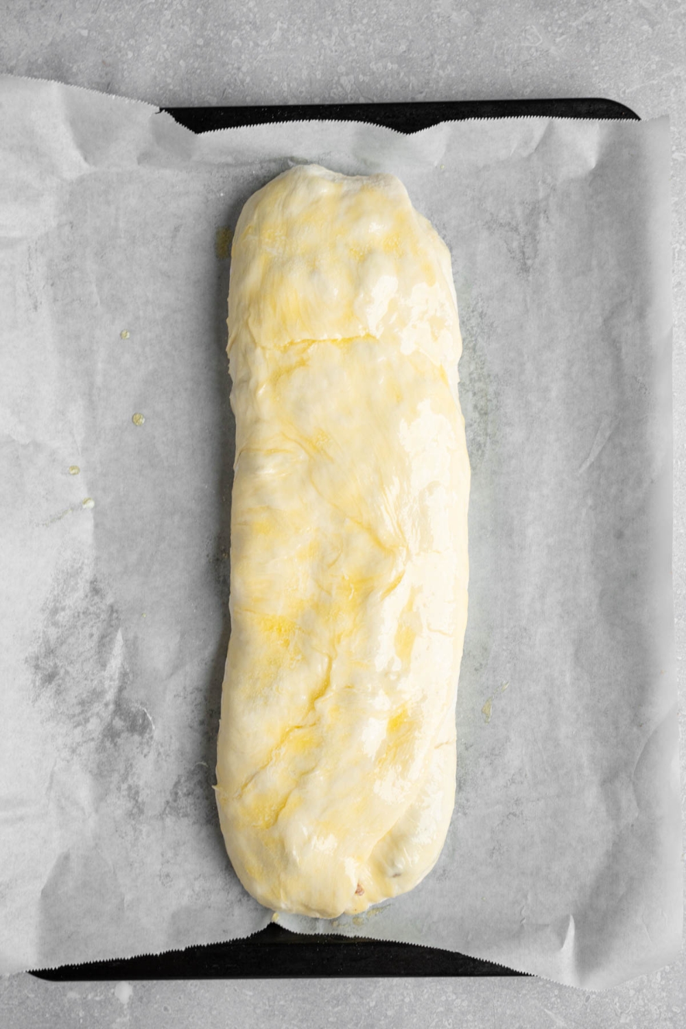 An uncooked loaf of garbage bread on a baking sheet lined with parchment paper. The baking sheet is on a white counter.