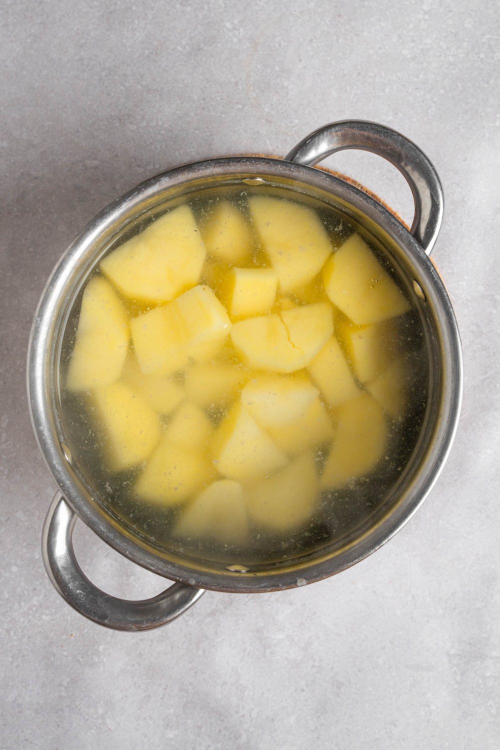 A pot of potatoes boiling in water. The pot is on a white counter.