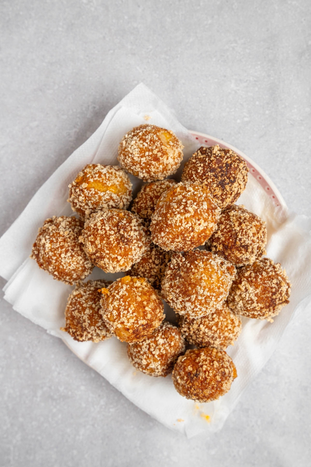 Fried mashed potato balls on a plate lined with paper towels. The plate is on a white counter.