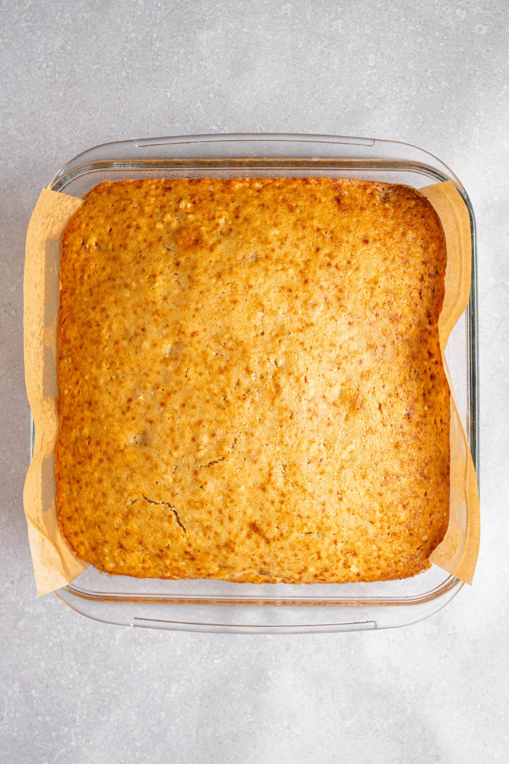 A glass baking dish lined with parchment paper with cooked Amish applesauce cake. The dish is on a white counter.