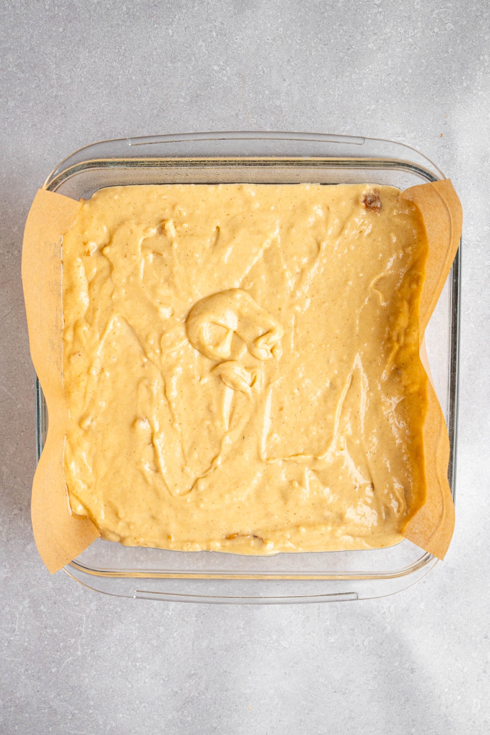 A glass baking dish lined with parchment paper with Amish applesauce cake batter. The dish is on a white counter.