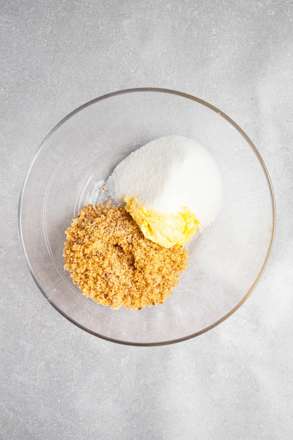 A glass bowl with sugar, brown sugar, and butter. The bowl is on a white counter.