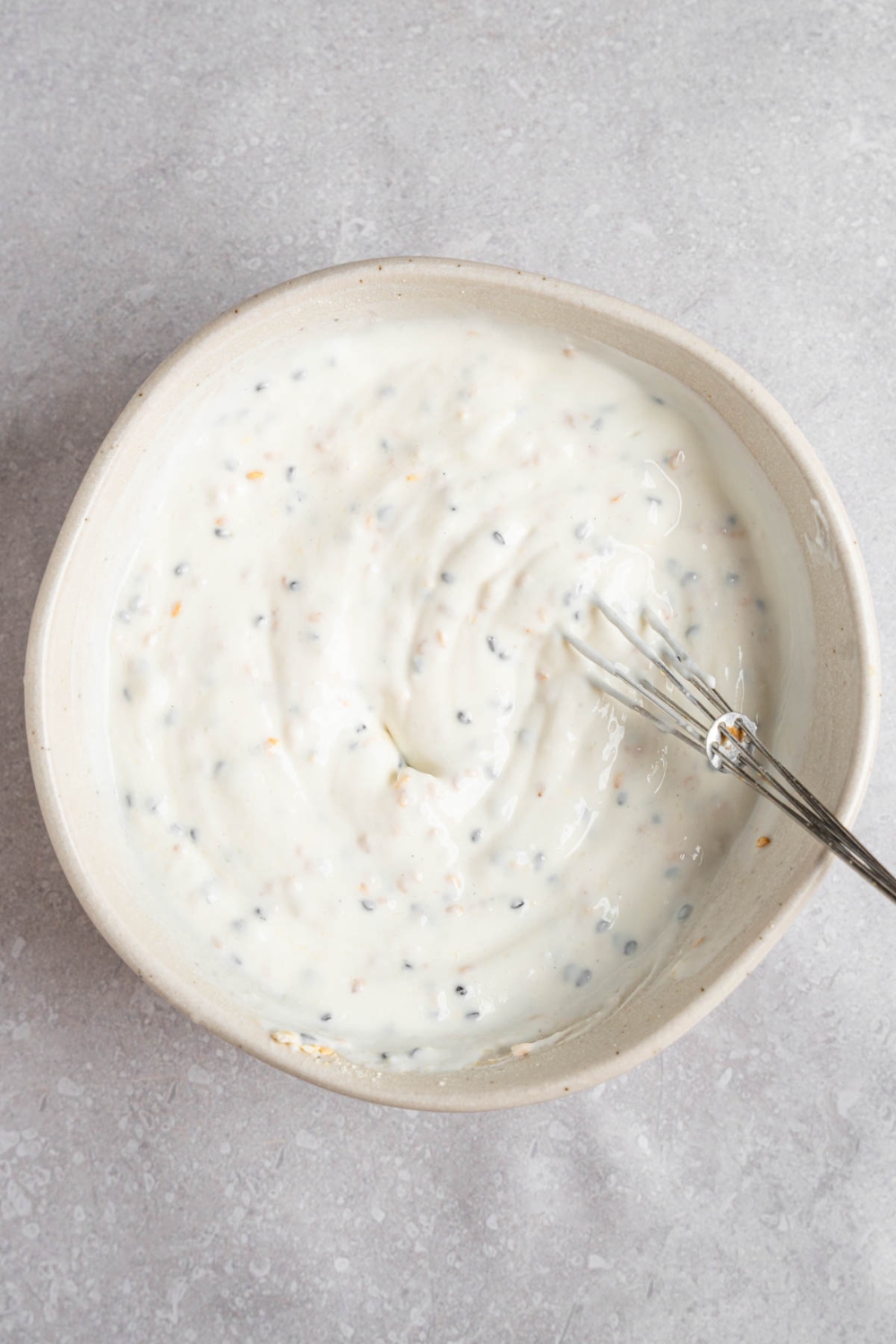 A whisk mixing bagel dip in a white bowl. The bowl is on a white counter.