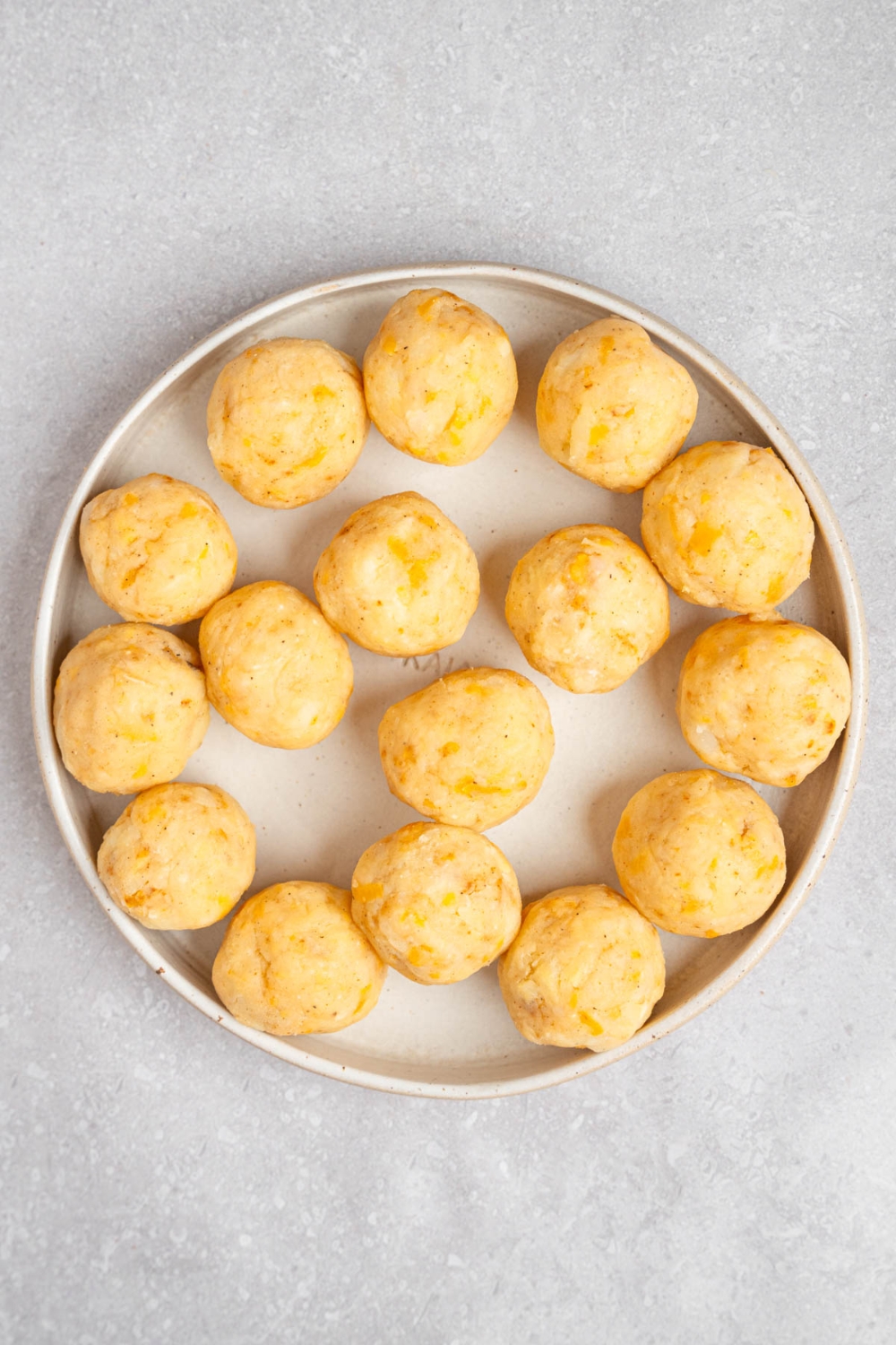 A plate of uncooked mashed potato balls. The plate is on a white counter.