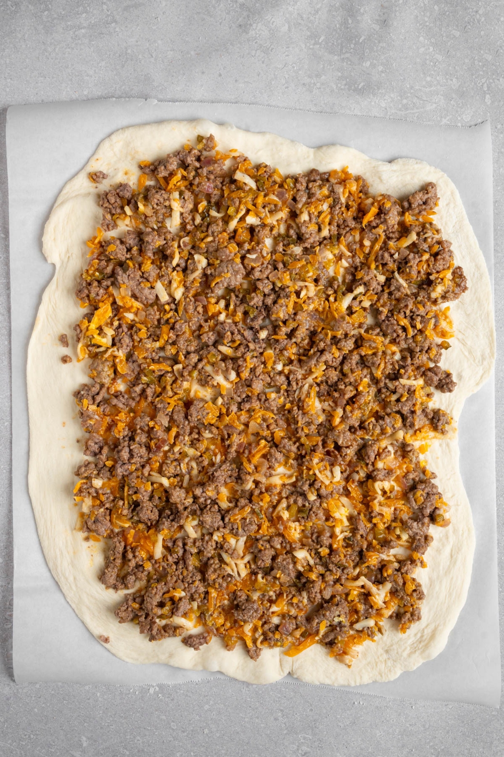 A beef mixture on top of rolled pizza dough. The dough is on a piece of parchment paper.