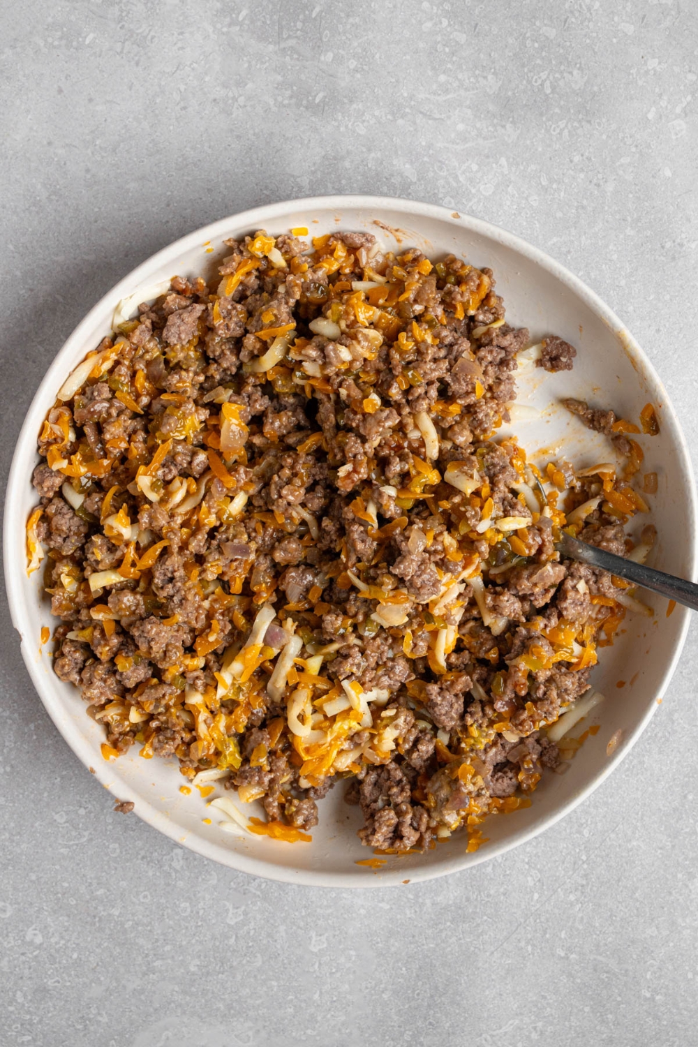 A white bowl with a spoon mixing a garbage bread beef mixture. The bowl is on a white counter.