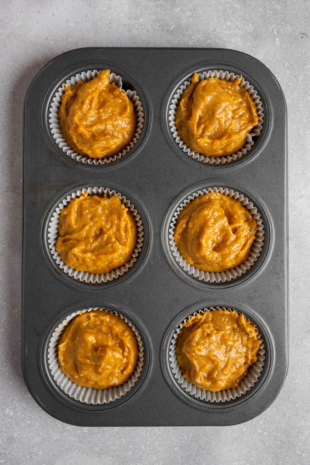 A muffin tray with six uncooked copycat Starbucks pumpkin muffins. The tray is on a white counter.