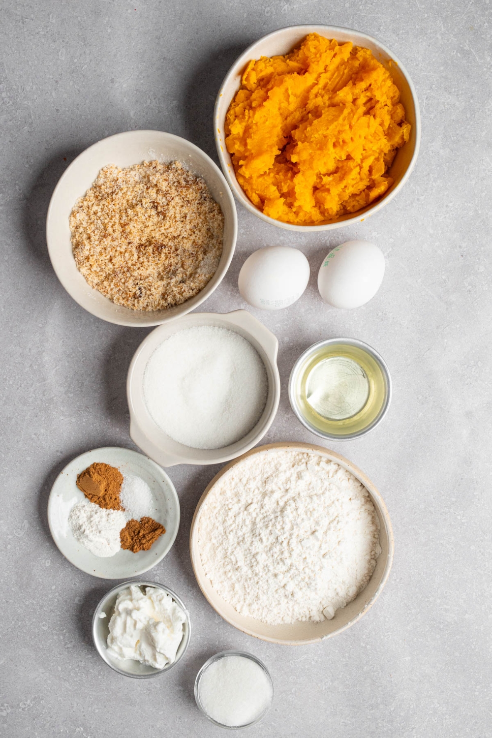 An overhead shot of several bowls in various sizes containing ingredients to make copycat Starbucks pumpkin muffins including pumpkin puree, eggs, brown sugar, white sugar, flour, vanilla, oil, and spices.