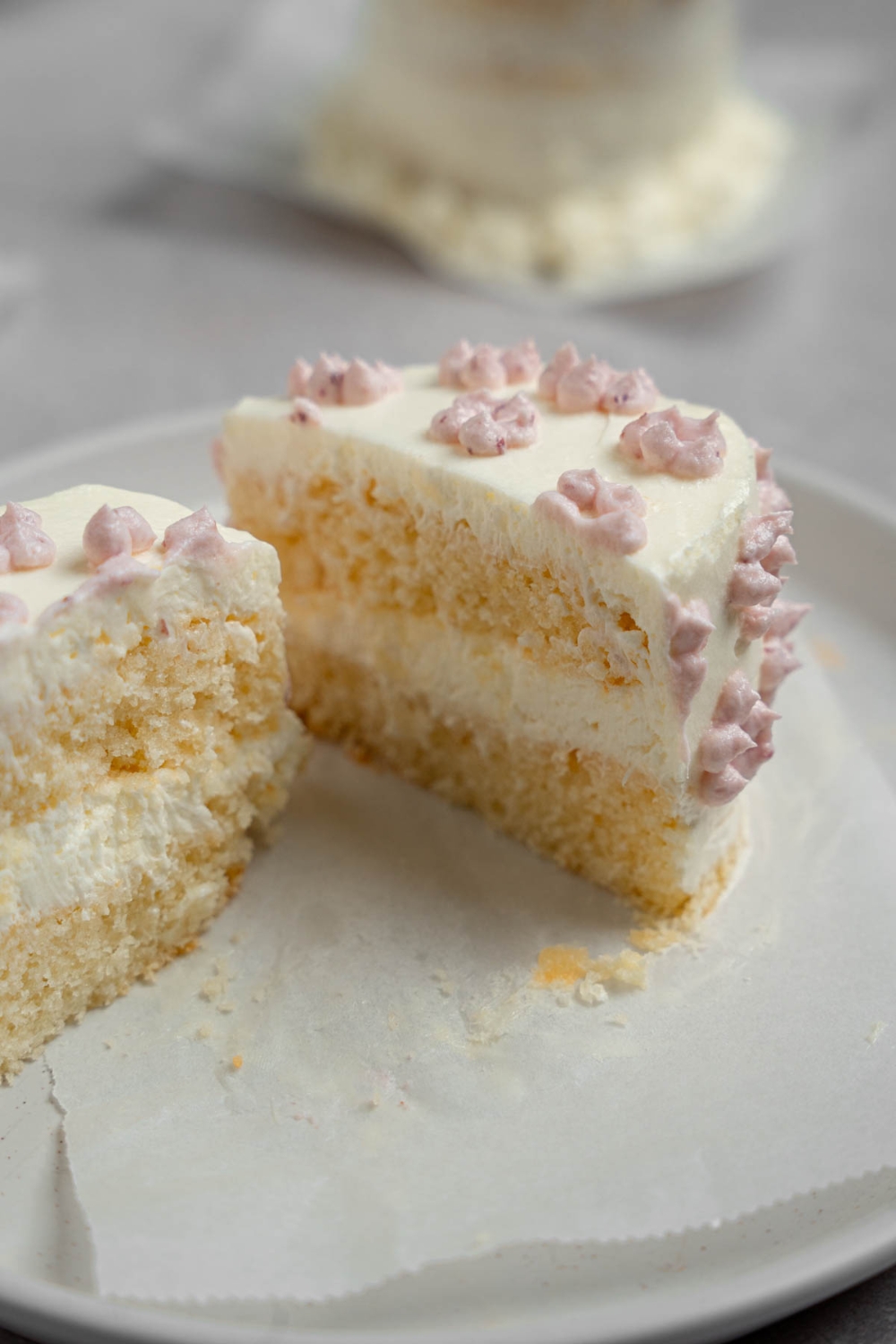 A vanilla lunch box cake with dotted purple icing sliced in half on a white plate The plate is on a white counter with another cake.