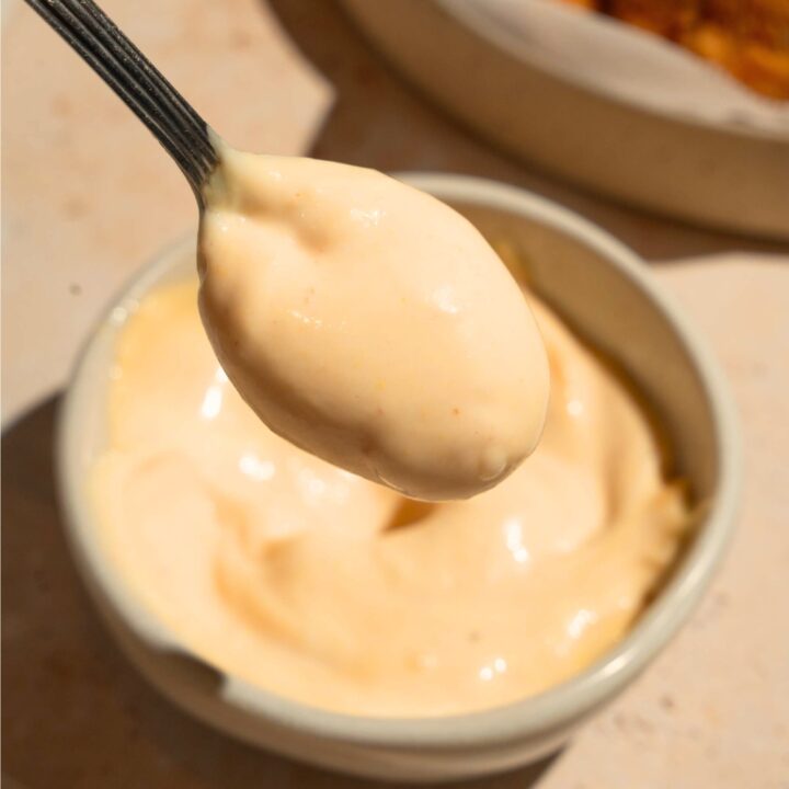 A spoon with chick-fil-a sauce on it being held over a bowl that is filled with the sauce.