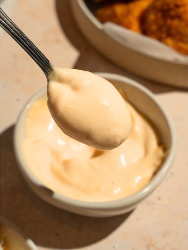 A spoon with chick-fil-a sauce on it being held over a bowl that is filled with the sauce.