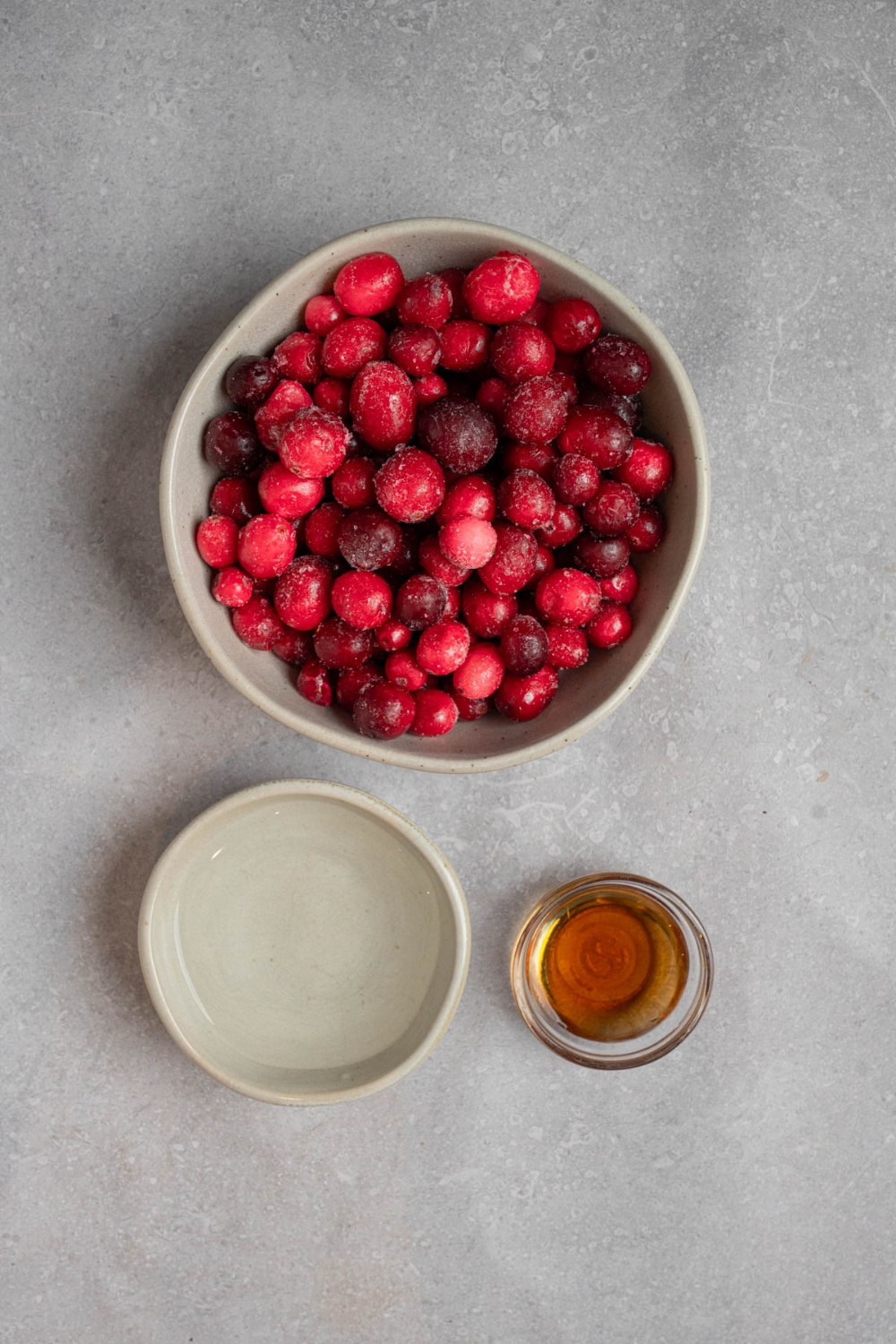 An overhead shot of three bowls with ingredients to make chokecherry pudding including chokecherries, water, and honey.